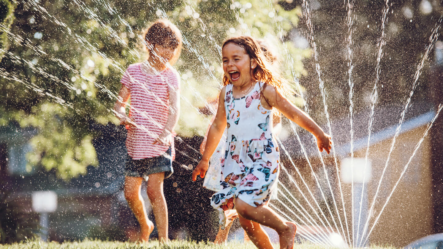 Two kids playing around the sprinklers